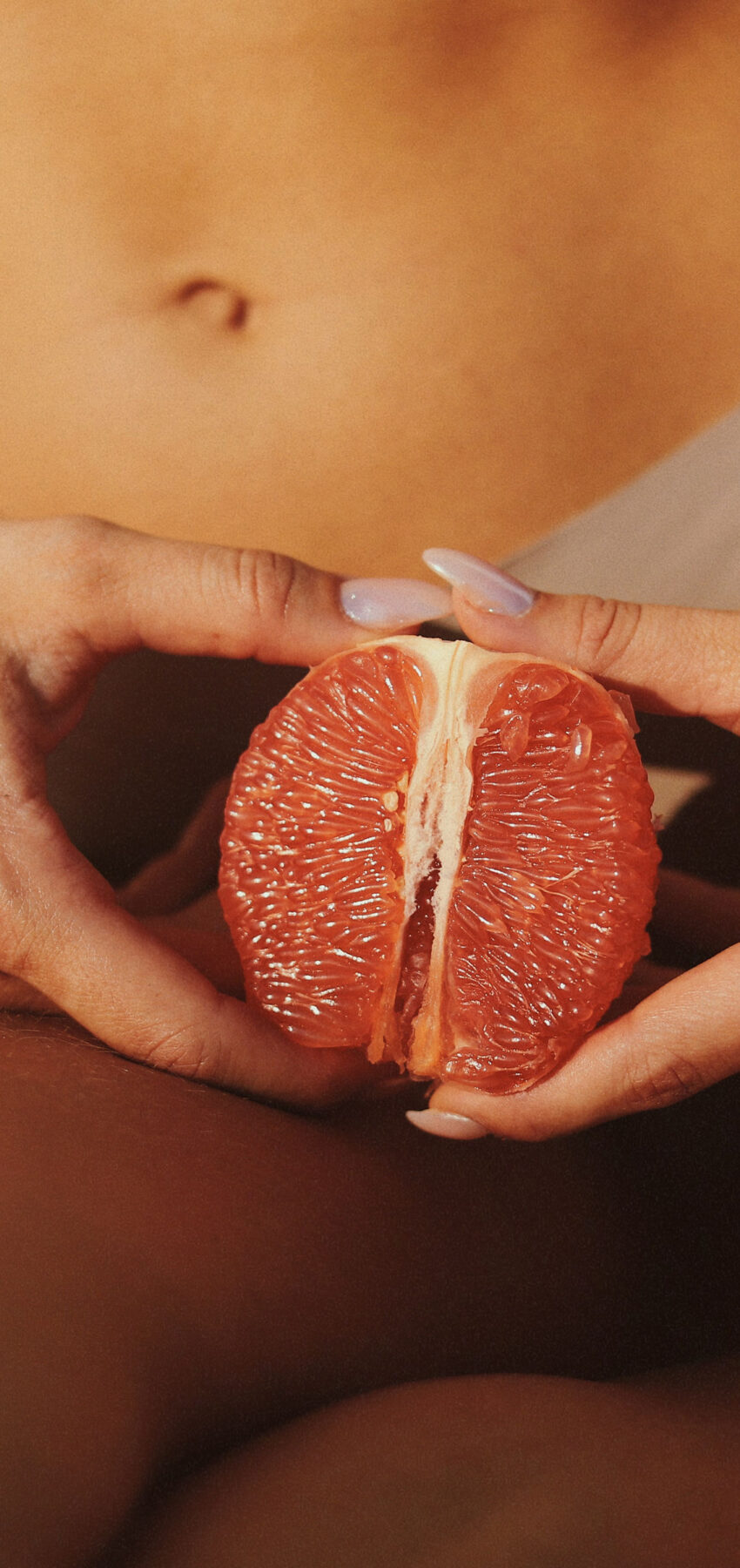 Žena drži polovicu grejpa ispred intimnog područja kao simbol ženskog intimnog zdravlja i njege.